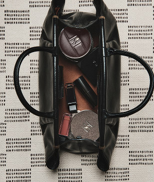 검은 핸드백 속에 헤라 2025 홀리데이 컬렉션의 다양한 메이크업 제품들이 가지런히 놓여 있어, 'ALL THAT GLAM' 룩을 위한 완벽한 준비를 보여준다.