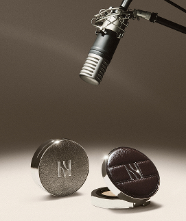 전문 마이크 아래에 헤라 로고가 새겨진 실버 콤팩트와 열린 다크 브라운 가죽 콤팩트가 놓여 'ALL THAT GLAM' 2025 홀리데이 컬렉션의 세련된 분위기를 보여준다.