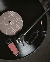 턴테이블 위 'All that Glam' 문구가 새겨진 LP판에 HERA 립 제품 두 개가 세련되게 놓여 2025 홀리데이 컬렉션의 글래머러스함을 연출한다.